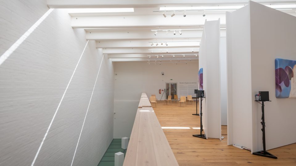 Výstavní prostor v Gočárově galerii je vysoký přes dvě patra, střešní průřezy se zastíněním tvoří působivou hru světel
